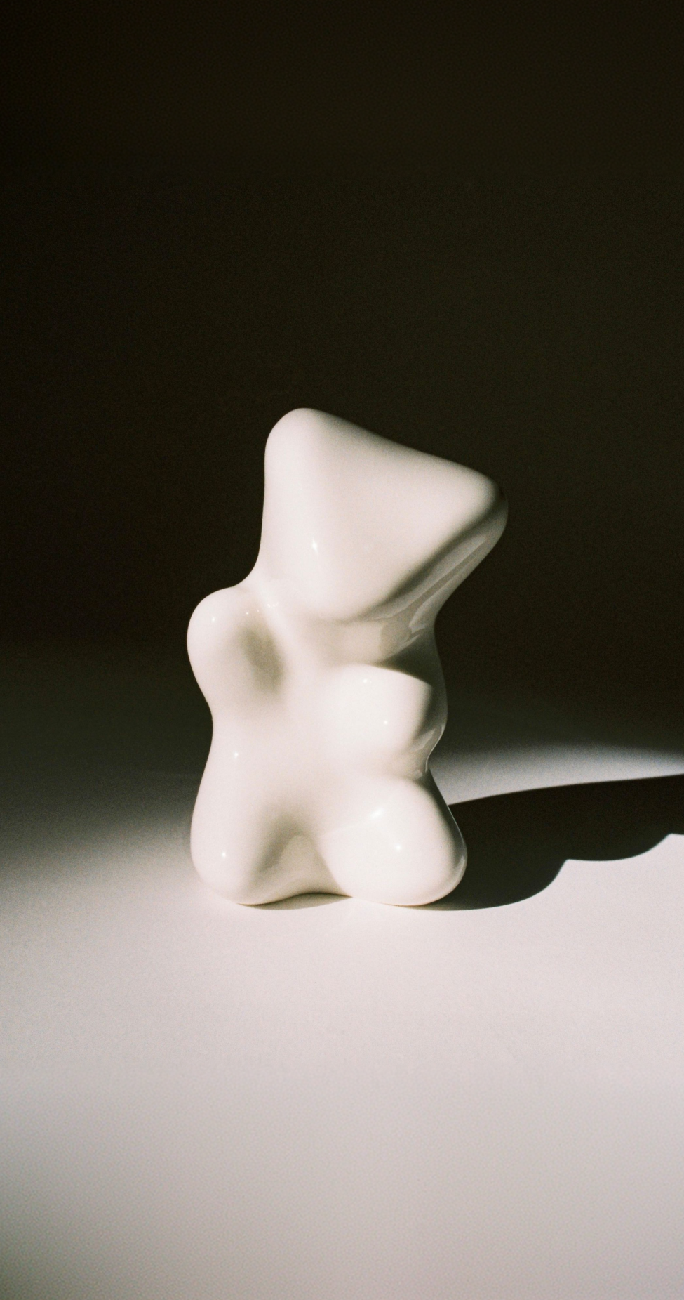 Abstract white ceramic sculpture on a dark background, with smooth, flowing curves and a polished surface.